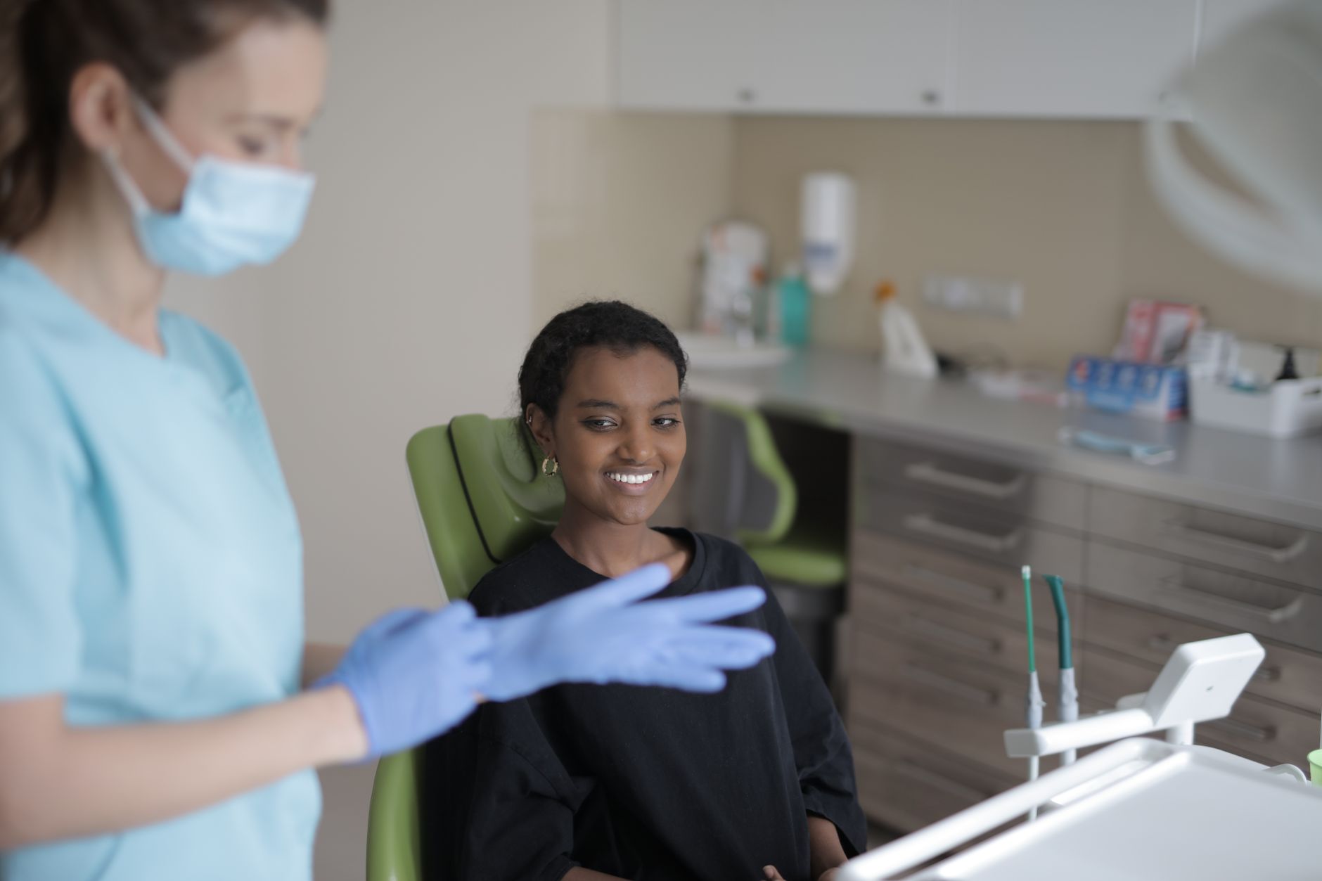 Positive young ethnic female patient smiling while sitting in dental chair and looking at dentist before treatment in mo